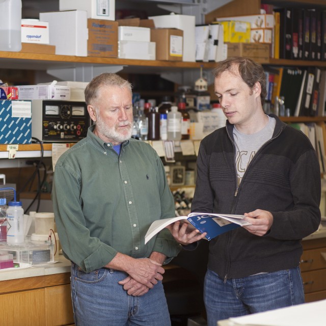 two researchers standing in lab reading a book