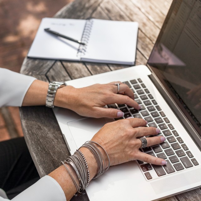 Person typing on laptop with notebook next to her